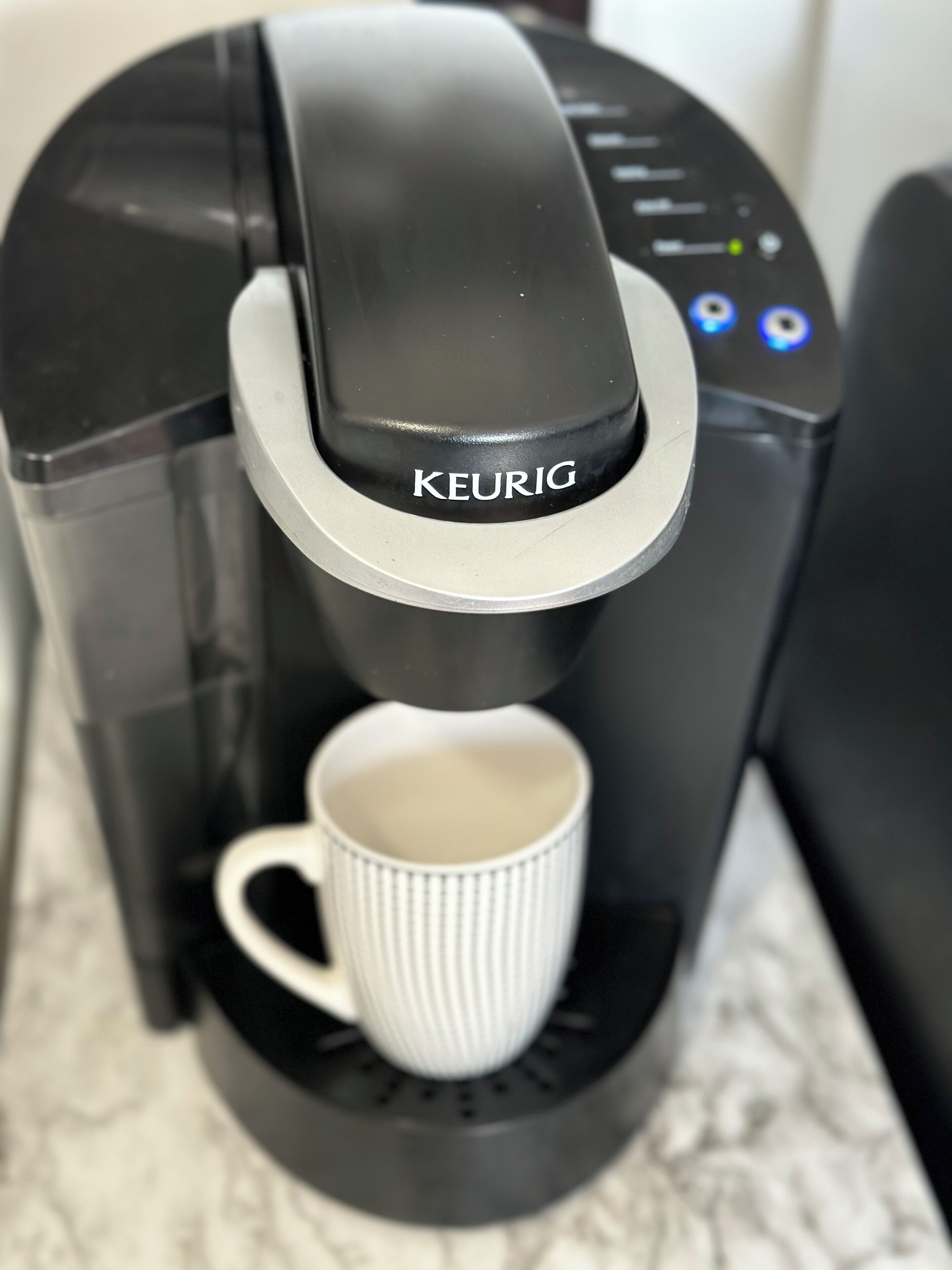 Una cafetera Keurg negra con una taza blanca debajo.