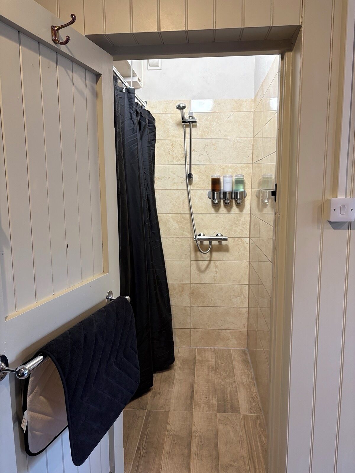 A narrow shower area with a glass door, a towel rack with a towel, and a showerhead mounted on the wall.