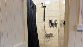 A narrow shower area with a glass door, a towel rack with a towel, and a showerhead mounted on the wall.