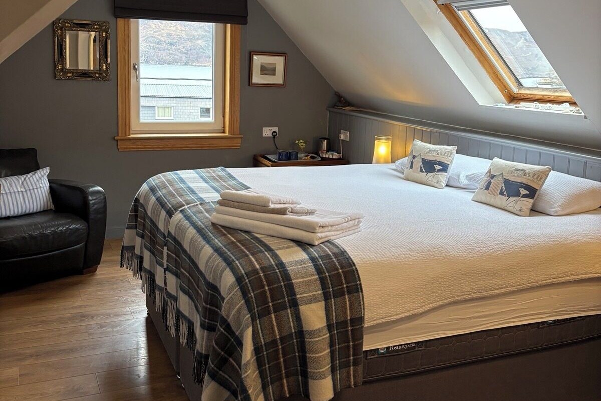 Une chambre avec un grand lit, une lucarne, un ventilateur de plafond et une fenêtre.