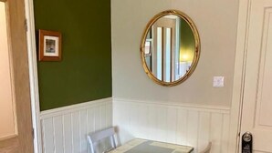 A room with a white table, two white chairs, a round mirror, and a green wall. - Highland Rooms - Room Only No Breakfast (Ullapool)