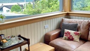 A cozy room with a wooden table, a leather sofa, and a window with a view of greenery and buildings. - Highland Rooms - Room Only No Breakfast (Ullapool)