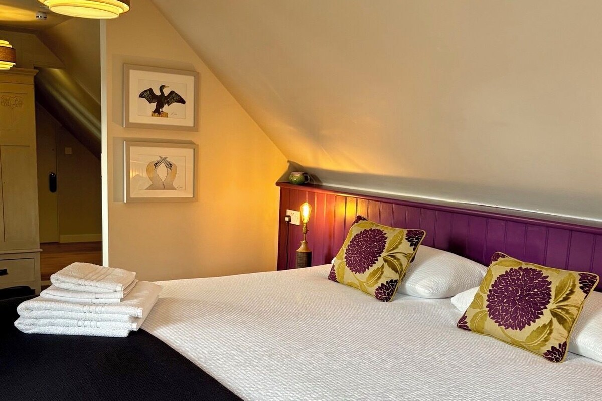Une chambre d’hôtel avec un lit, un luminaire suspendu, un escalier et des œuvres d’art encadrées accrochées au mur.