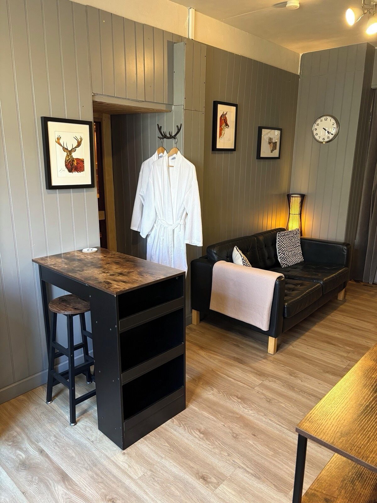 A room with a wooden bar, a black leather sofa, a framed deer head, and a clock on the wall.