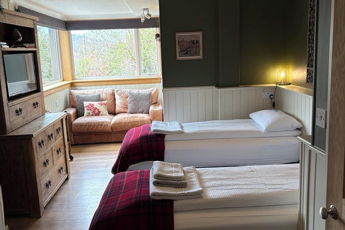 A cozy room with a sofa, two beds, a TV, and a window.