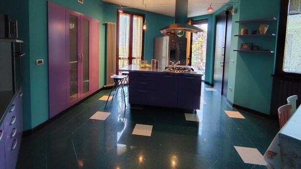 A modern kitchen with teal walls, a central island, and a dining area with chairs.