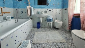 A bathroom with a blue and white tiled floor, a bathtub, a sink, a toilet, and a small stool.