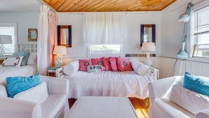 Ein gemütliches Schlafzimmer mit Holzbalkendecke, einem Bett mit rosa-weißer Bettwäsche, zwei weißen Stühlen und einem kleinen Tisch mit einer Lampe.