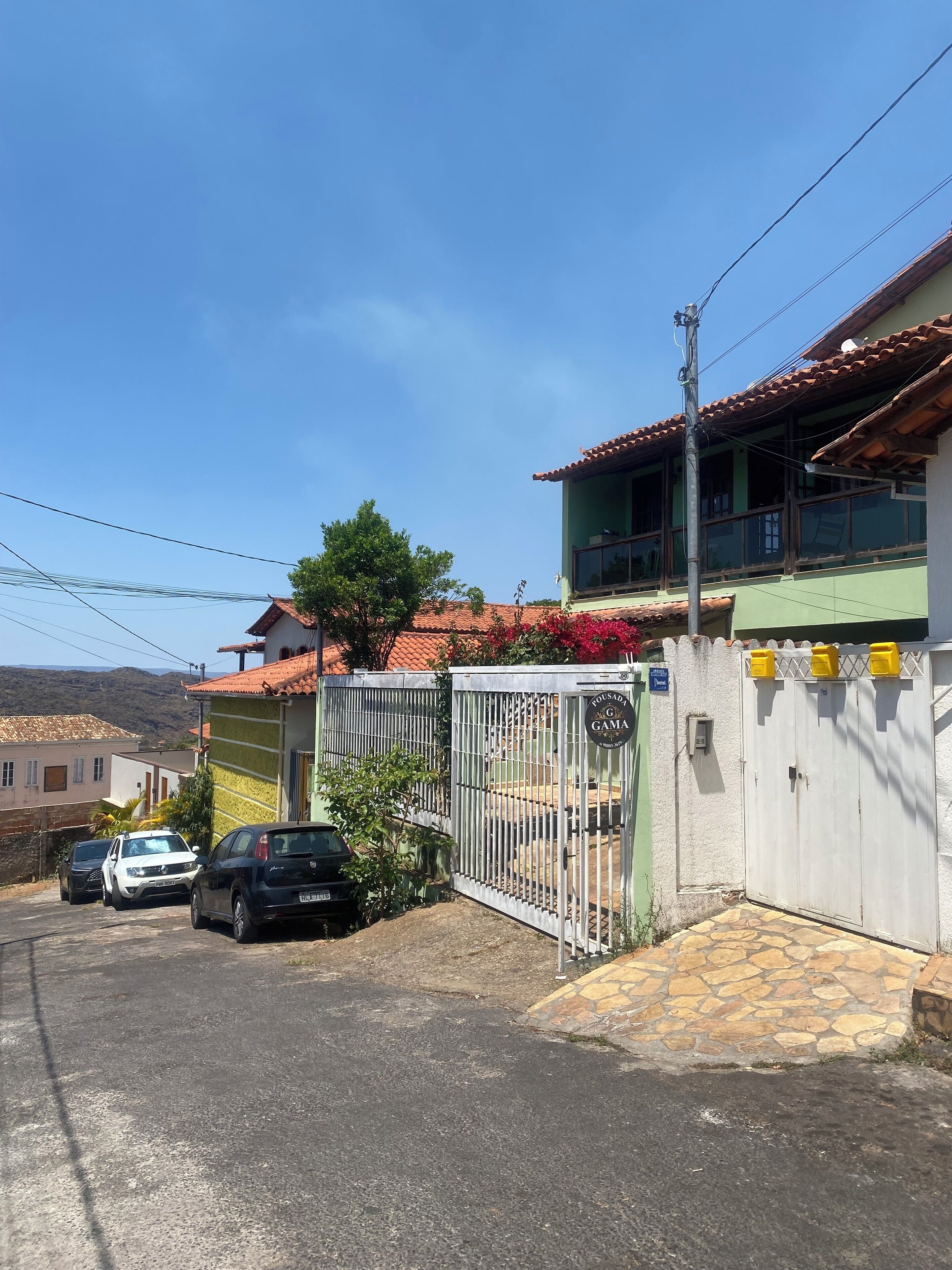A gated residential area with a paved driveway, parked cars, and a building with a tiled roof.