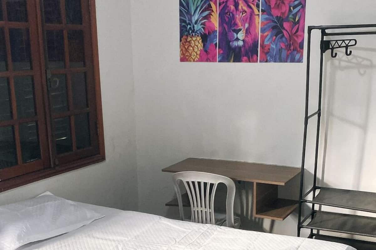 A bedroom with a bed, a desk, a chair, and a window.