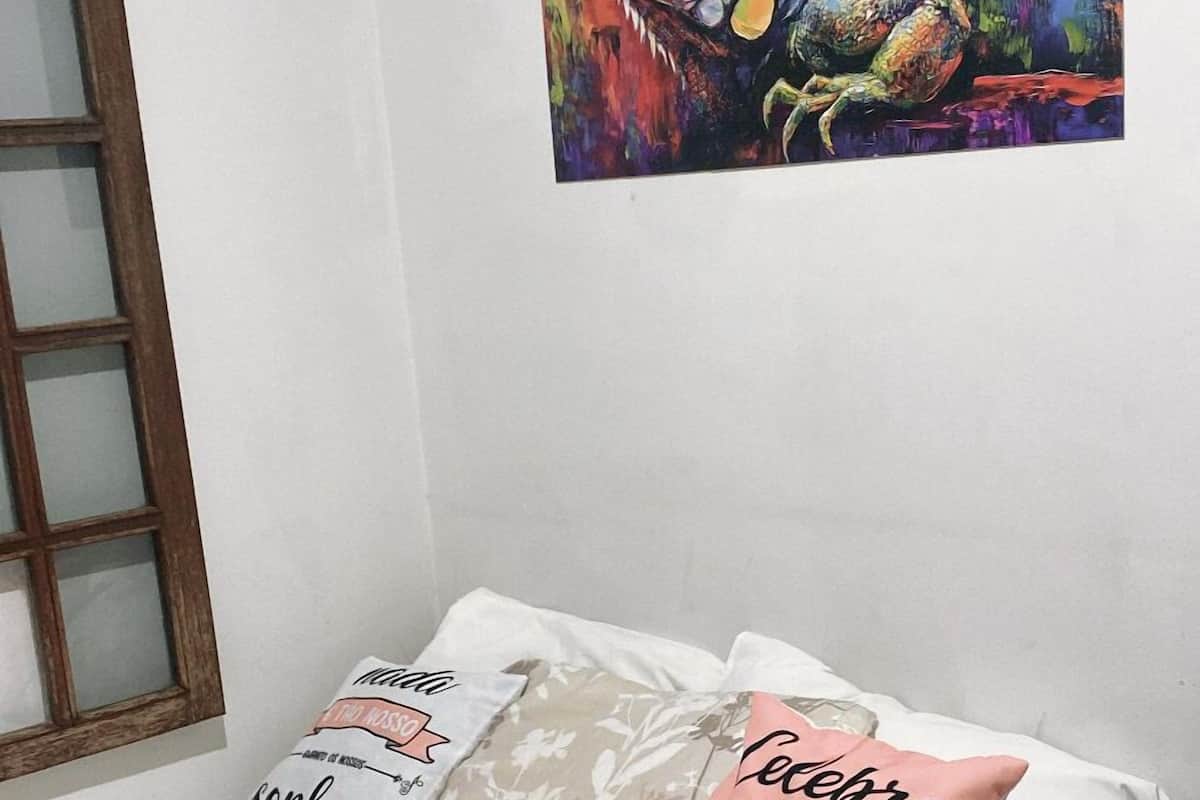 A bedroom with a bed, two pillows, a remote control, and a colorful painting on the wall.