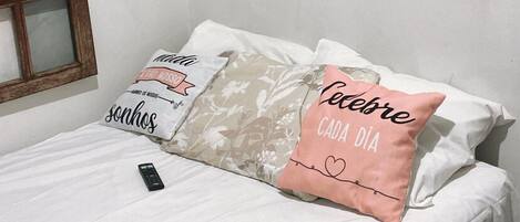 A bedroom with a bed, two pillows, a remote control, and a colorful painting on the wall.