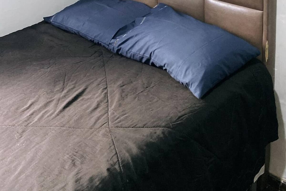 A bedroom with a brown headboard, two blue pillows, and a dark-colored bedspread.