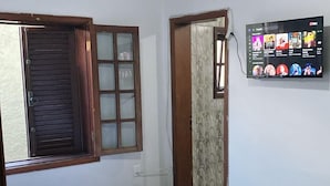 A bedroom with a bed, a window with wooden shutters, a wall-mounted TV, and a ceiling fan. - Pousada Gama (Diamantina)