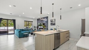 A modern kitchen with a central island, a dining area with a blue sofa, and a large window with a view.