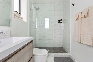 A modern bathroom with a white marble shower, a white toilet, and a beige towel hanging on the wall.