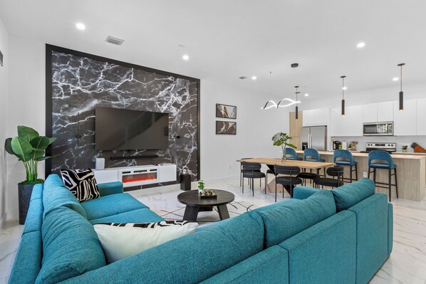 A modern living room with a large flat-screen TV, teal sofas, and a marble accent wall.