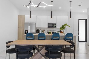 A modern kitchen with white cabinets, a central island with blue chairs, and pendant lighting.