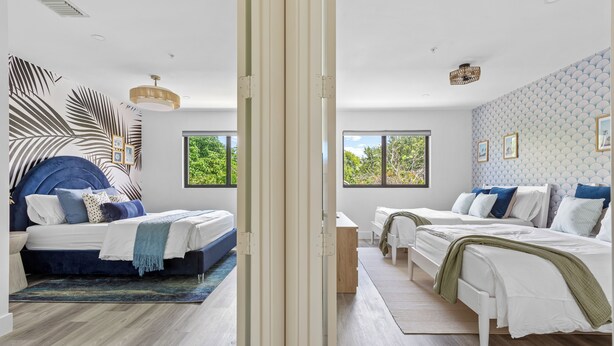 A modern bedroom with two beds, a large window, and a decorative wall.