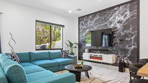 A modern living room with a teal sofa, a marble-patterned wall, a flat-screen TV, and a fireplace.