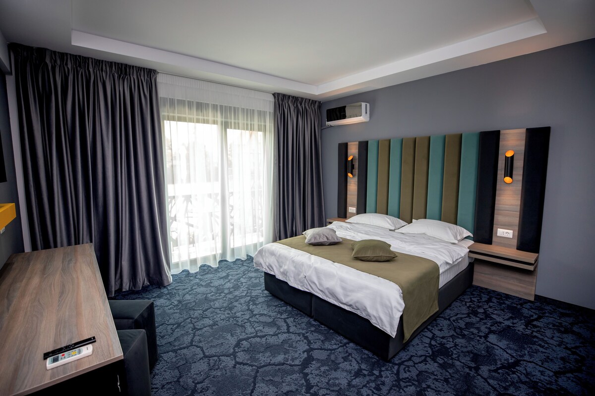 A hotel room with a bed, a desk, and a large window with curtains.