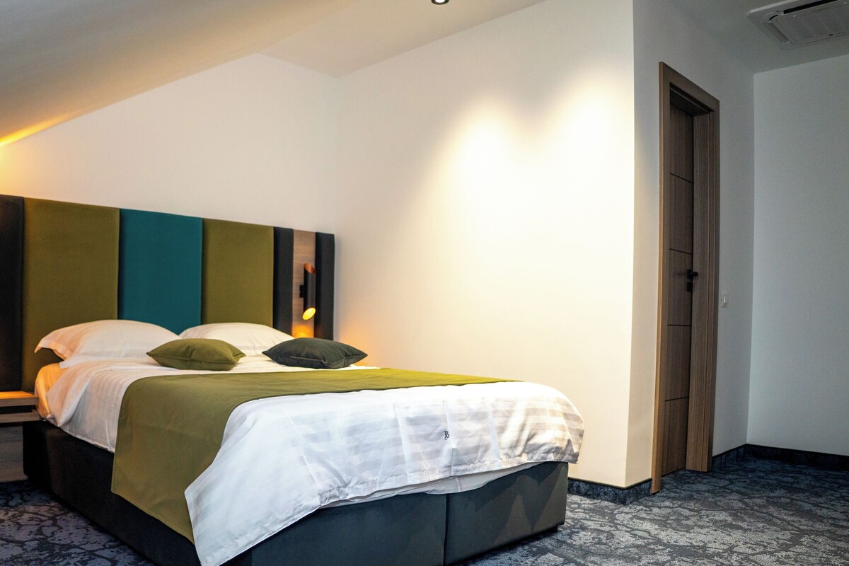 A modern hotel room with a bed, a nightstand, a wall-mounted light, and a door.