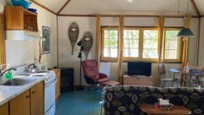 Cocina pequeña con estufa, pileta y alacenas de madera. En la sala de estar, hay un sillón rojo y un sofá estampado.