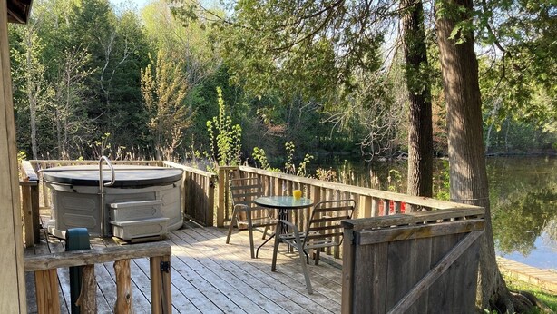 Una terraza de madera con un jacuzzi, una mesa y sillas con vistas a un lago.