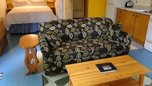 Una habitación compacta con cama, sofá, una pequeña mesa de madera y un rincón de cocina.