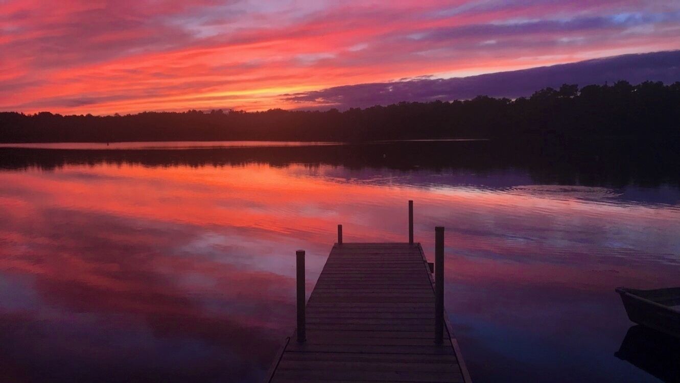 A wooden pier extending into calm water with a sunset in the background.