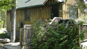A wooden cabin with a green roof, a porch, and a grill area.