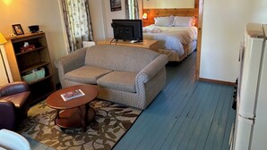 A cozy room with a sofa, a small table, a wooden bookshelf, a bed, and a TV.