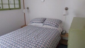 Et soveværelse med en seng, to sengeborde med lamper, et vindue med grøn ramme og et grønt skab.