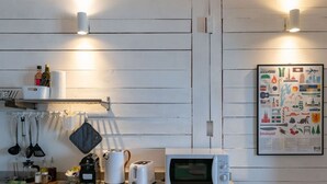 Een keuken met een wit aanrecht, een Prolex magnetron, een broodrooster en een waterkoker. Er hangen keukengerei en een plank met flessen en een pak keukenpapier.