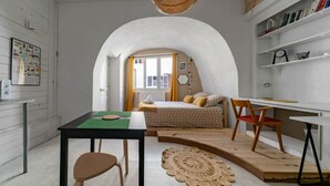 Een kleine kamer met een bed, bureau en stoel, met een wit gewelfd plafond en een klein raam met gordijnen.