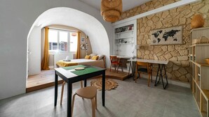 Een gezellige kamer met een gebogen witte muur, een stenen muur met een wereldkaart, een houten tafel met stoelen en een hangende rieten lamp.
