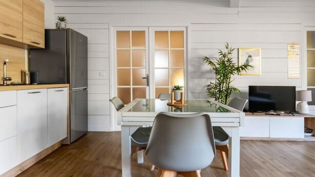 Een moderne keuken met houten kastjes, een inbouwkoelkast en een eethoek met een glazen tafel en stoelen.