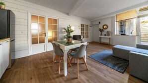 Een moderne keuken met witte kasten, een eettafel met stoelen, een koelkast en een raam met jaloezieën.