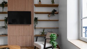 A modern living room with a wooden slat wall, a flat-screen TV, wooden shelves with plants, a round coffee table, and a white sofa. - Air-cond and designer apartment (Vichy)