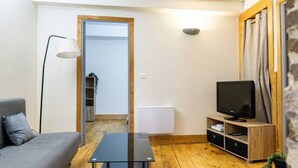 A modern living room with a wooden floor, a grey sofa, a glass coffee table, a television on a wooden stand, and a lamp. - Le Cosy - 11 Rue de la Boucherie - Clermont (Clermont-Ferrand)