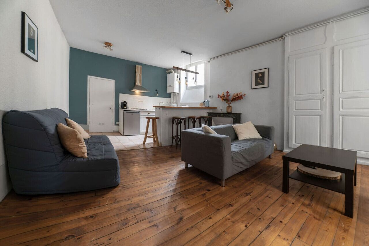 Un salon moderne avec un plancher en bois, deux canapés, une table basse et une cuisine en arrière-plan.