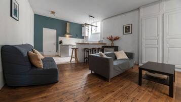 Un salon moderne avec un plancher en bois, deux canapés, une table basse et une cuisine en arrière-plan.