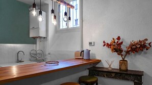 Een keuken met een houten aanrecht, een spoelbak en een raam. Er hangen lampen, staat een broodrooster en een vaas met gedroogde bloemen op het aanrecht.