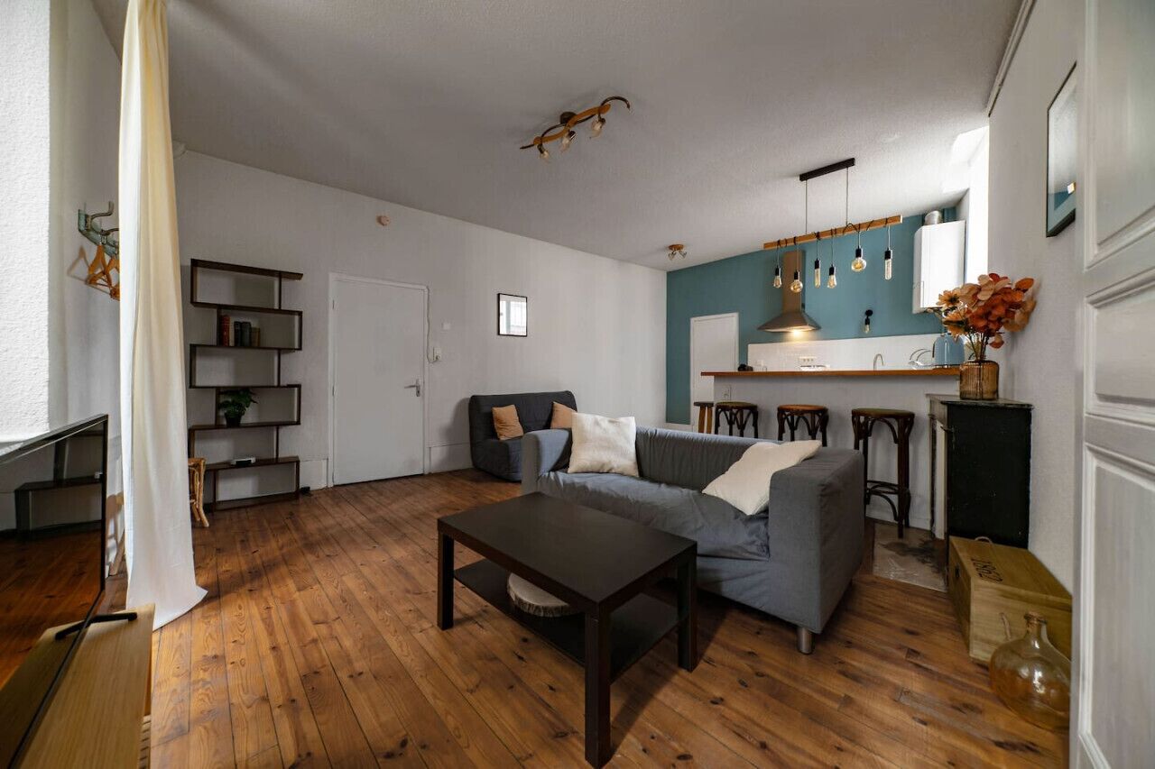 Ein Wohnzimmer mit einer Couch, einem Couchtisch und einer Küchenzeile mit Fenster und Pendelleuchten.