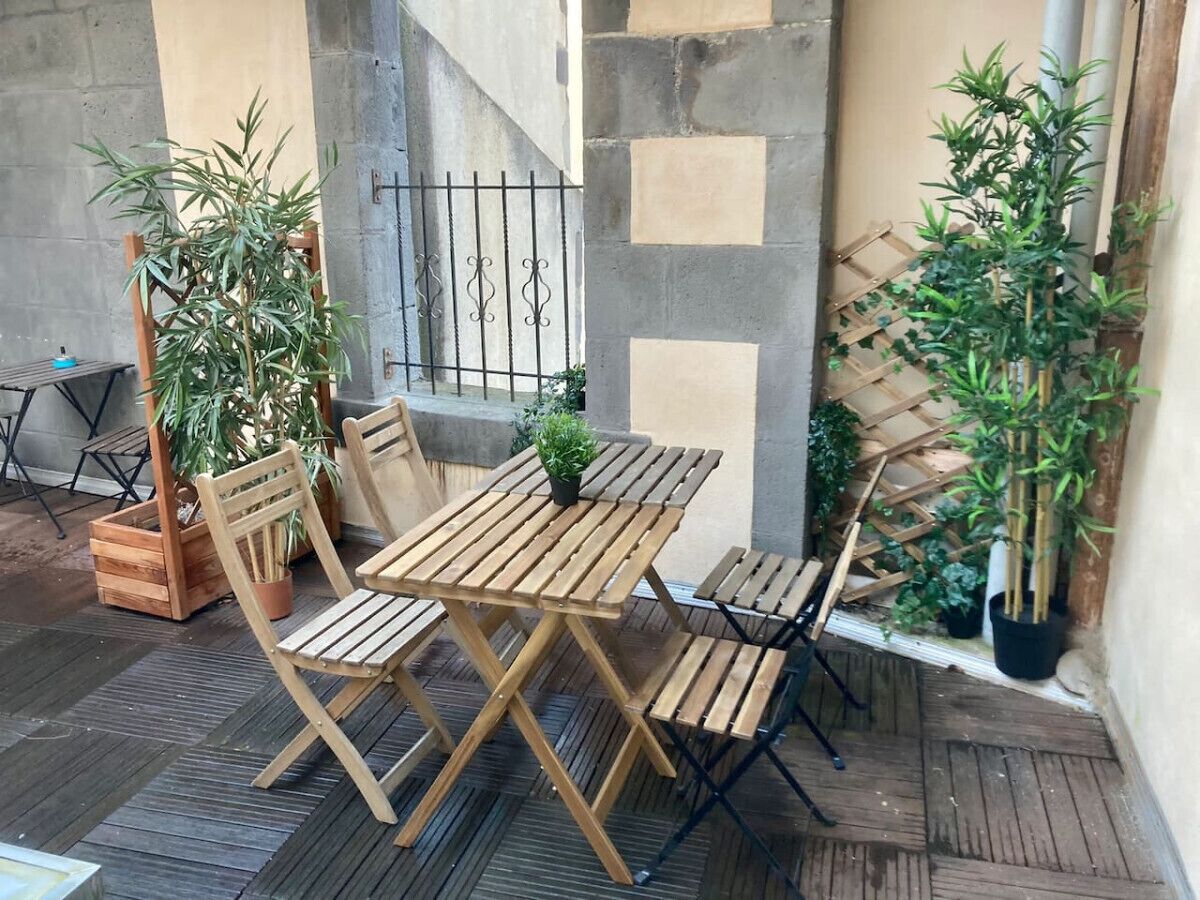 Een houten tafel met stoelen op een terras, met potplanten en een metalen hek.