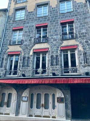 A building with a stone facade, multiple windows with red awnings, and a sign reading "BISTRO VENITIEN" indicating a restaurant. - T1 cocooning with terrace (Clermont-Ferrand)