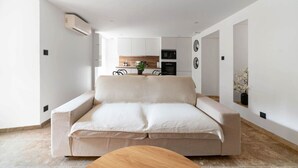 Ein modernes Wohnzimmer mit einer Couch, einem Holztisch und einer Küche im Hintergrund.