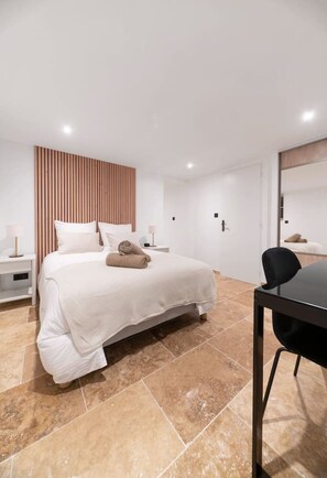 A modern hotel room with a large bed, a wooden panel wall, a small table with a chair, and a bathroom visible through a glass door. - Air-cond and designer apartment with terrace (Vichy)
