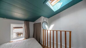 Un dormitorio con tragaluz, cama, barandilla de madera y ventana.