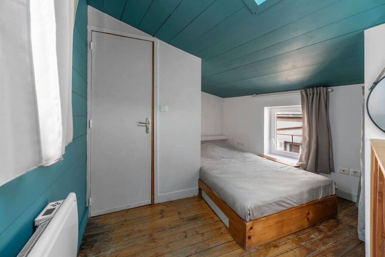 A bedroom with a single bed, a window with curtains, a door, and a radiator.